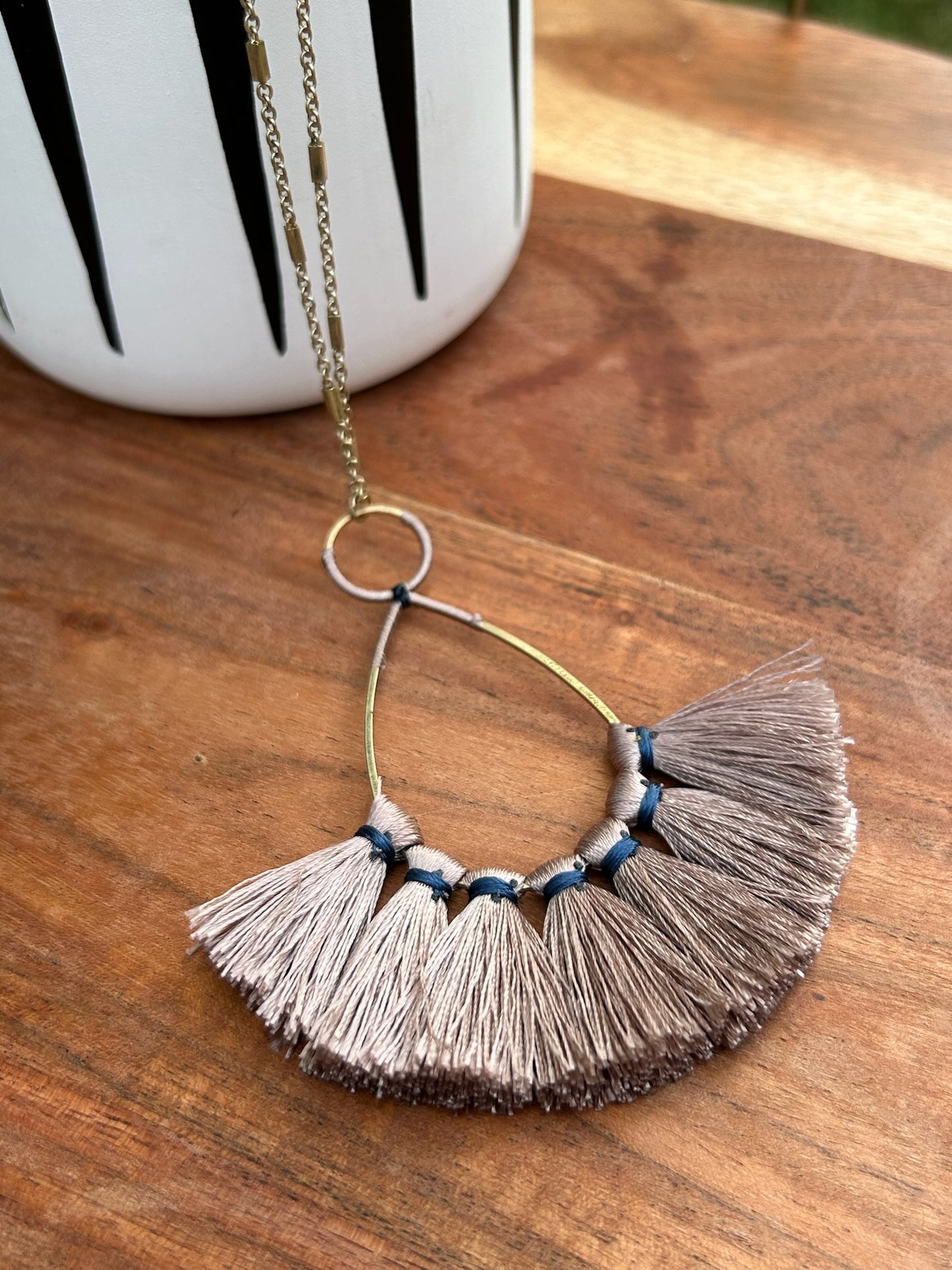 A Pale Light Fringe Necklace with navy blue thread accents, displayed on a rusted metal surface. The necklace features a sterling silver chain looped through a metal ring.