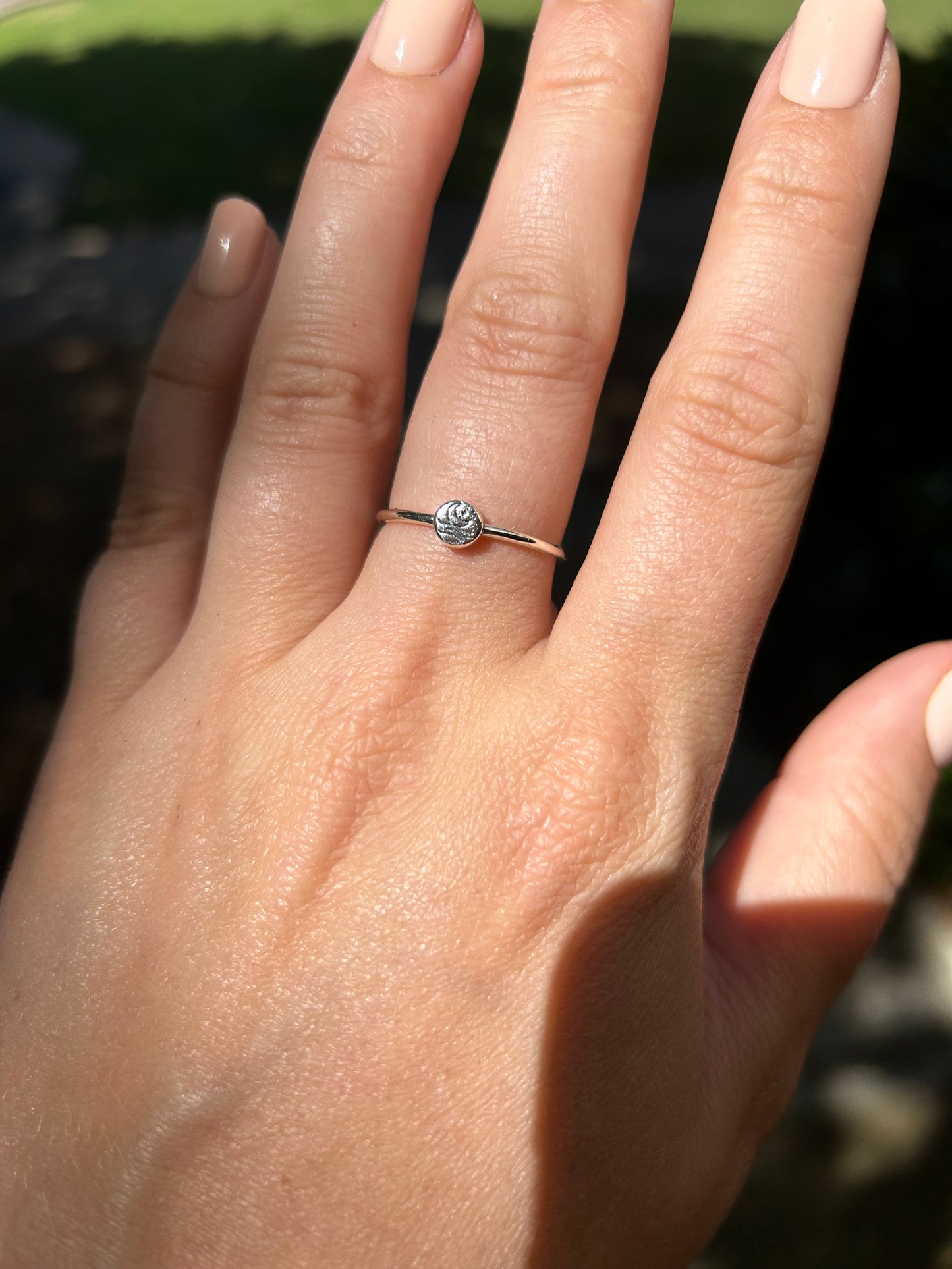 A close-up image of a Canyon Jewelry Moon Ring with a small, intricate design, resting on a patch of vibrant green moss on a textured, reddish surface.