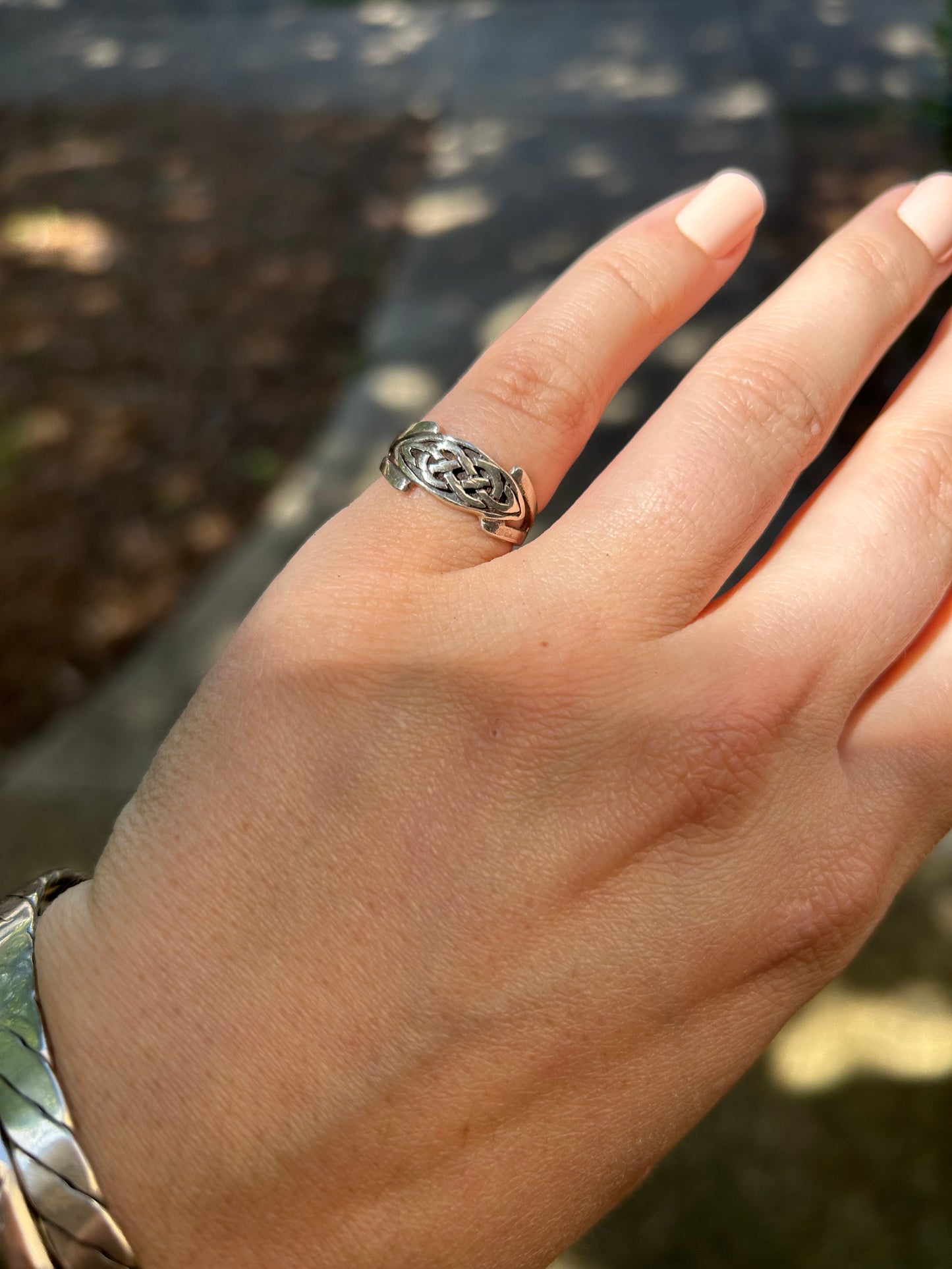 Close-up of a silver Canyon Jewelry boho celtic knot ring resting on a mossy surface, with a soft-focus background that includes indistinct natural elements.