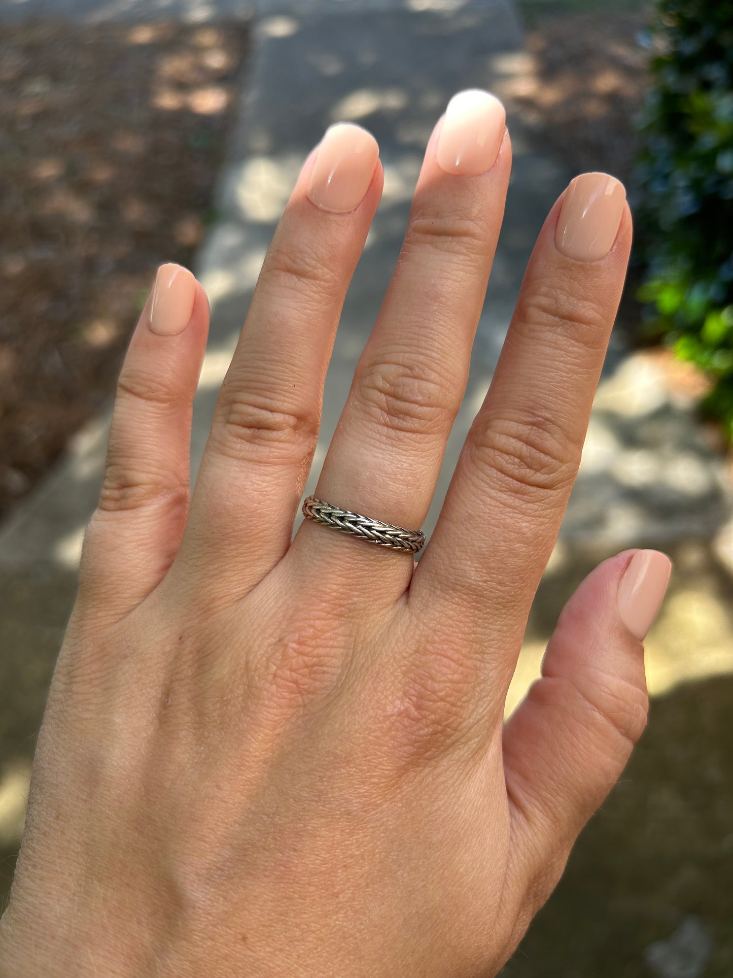 Close-up of a Canyon Jewelry sterling silver braided chain ring resting on green moss, with a blurred background emphasizing the detailed texture of the ring and moss surface.