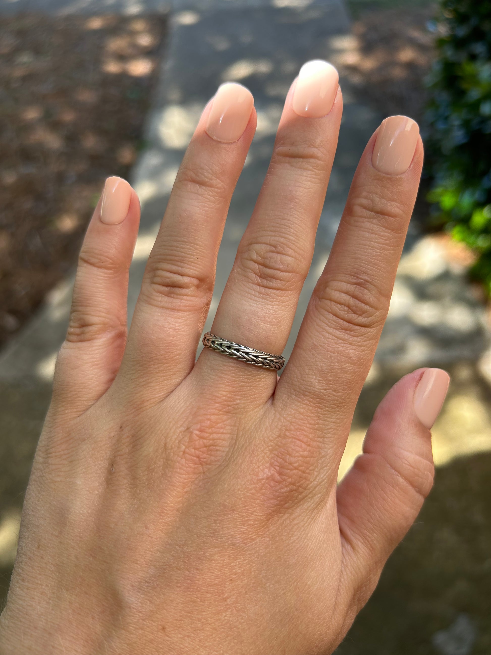 Close-up of a Canyon Jewelry sterling silver braided chain ring resting on green moss, with a blurred background emphasizing the detailed texture of the ring and moss surface.