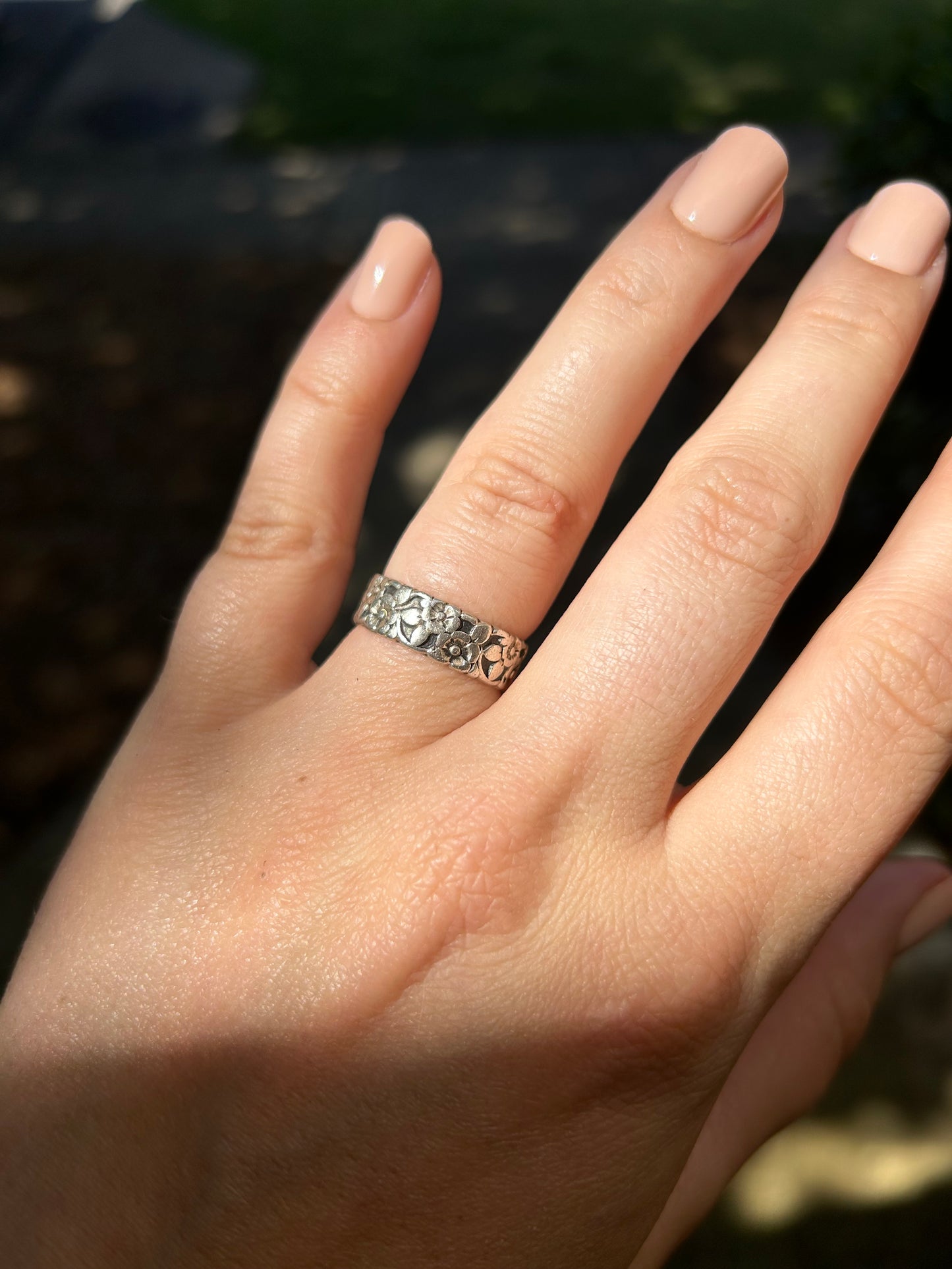 A close-up of a Flora Ring by Canyon Jewelry, a vintage silver ring with delicate flower engravings, resting on a bed of vibrant green moss with a soft, blurred background.