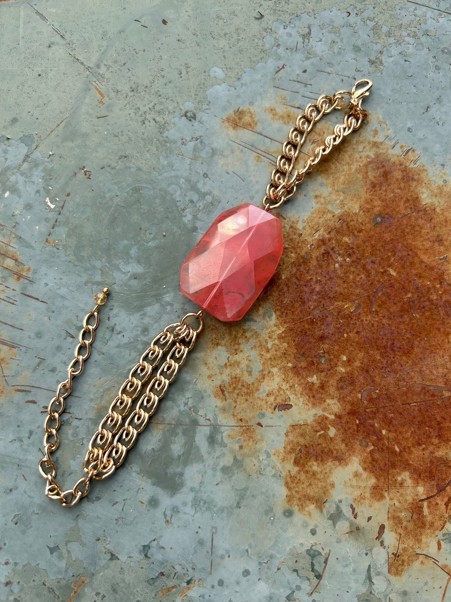 A Hillier Bracelet on a golden chain, resting on a wooden surface next to decorative ceramic vases and a white fringed boho cloth.