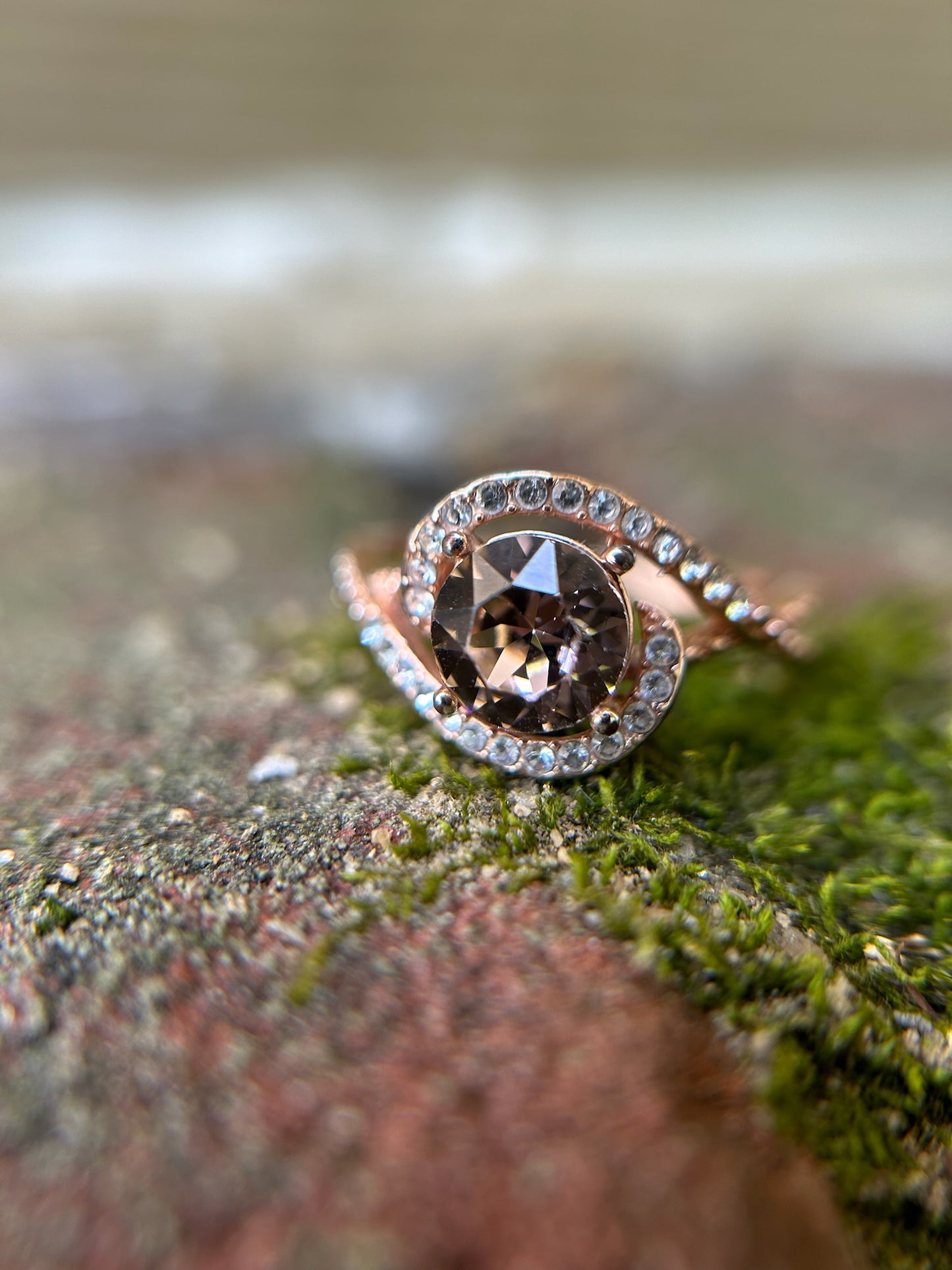 Close-up of a sparkling round-cut Hold Me Closely Ring from Canyon Jewelry, with a sterling silver band, encircled by smaller diamonds. It rests on a moss-covered surface, creating a natural contrast.