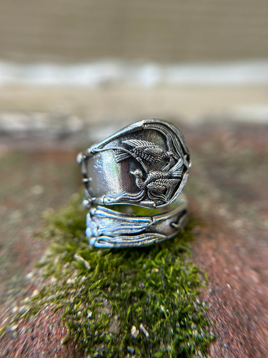 Close-up image of a Audrey Spoon Ring from Canyon Jewelry with intricate dragon engravings, resting on a mossy surface, with a blurred background.