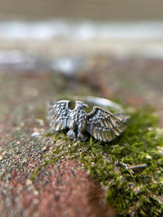 Close-up of a Canyon Jewelry sterling silver Eagle Ring resting on a mossy surface, focusing sharply on the detailed wings and body of the eagle, with a softly blurred background.