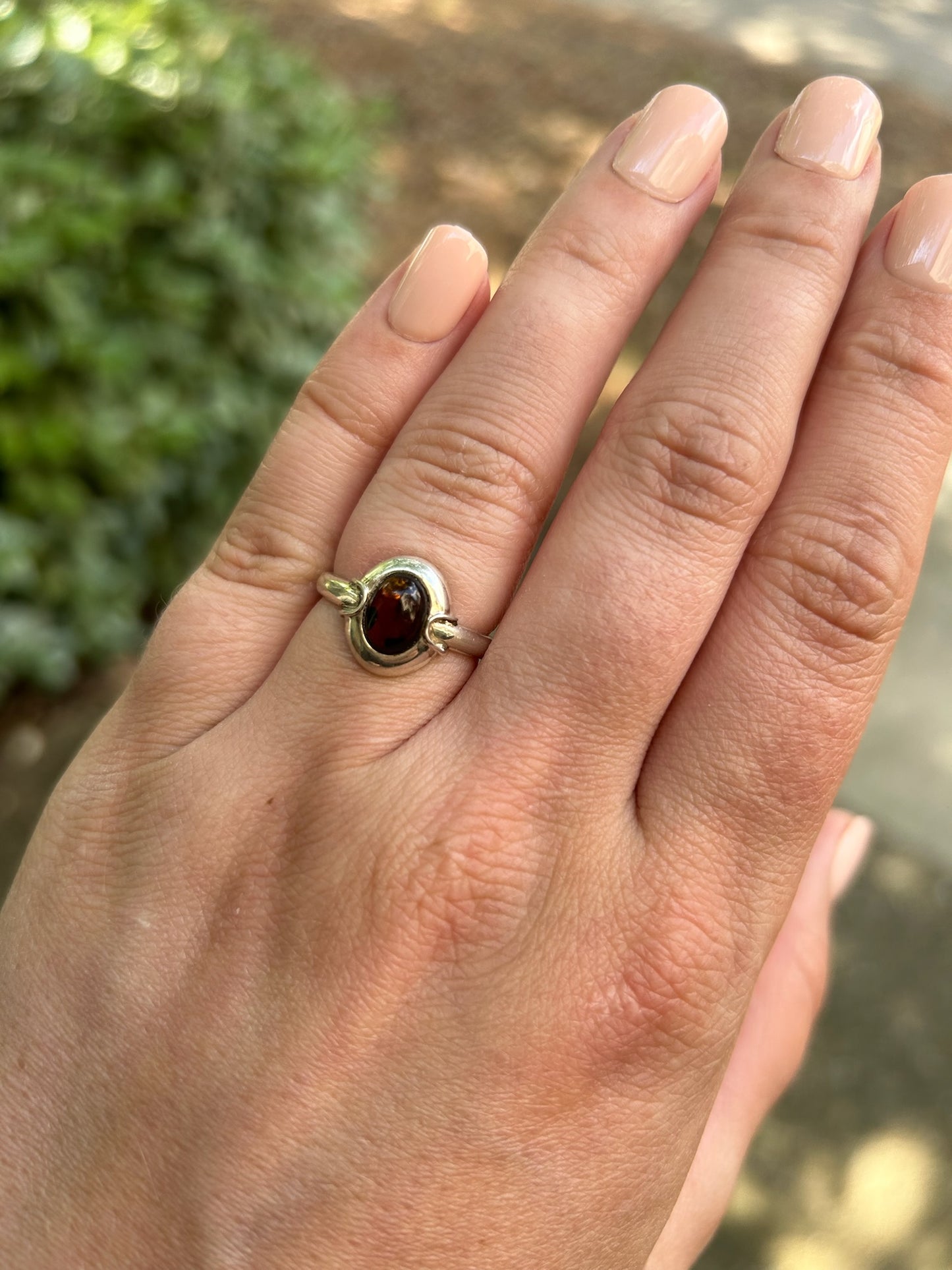 Close-up image of a vintage Ladybug Ring from Canyon Jewelry with an amber gemstone, set against a background of moss-covered stone. The focus is sharp on the gemstone, highlighting its rich, deep color.