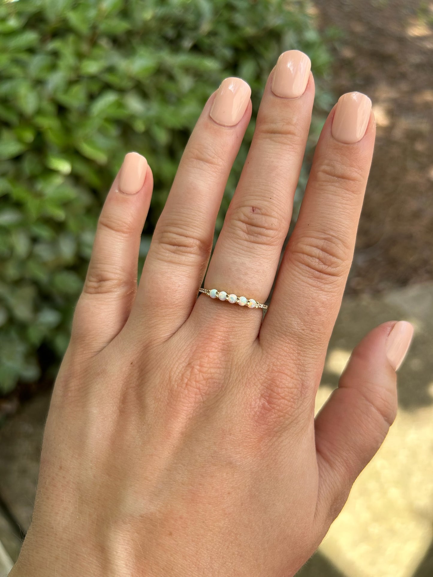 Close-up of a delicate Opalescence Ring with five opal stones, set on a moss-covered rock, showcasing Canyon Jewelry's boho jewelry style, with a blurry background emphasizing the gemstones' iridescence.