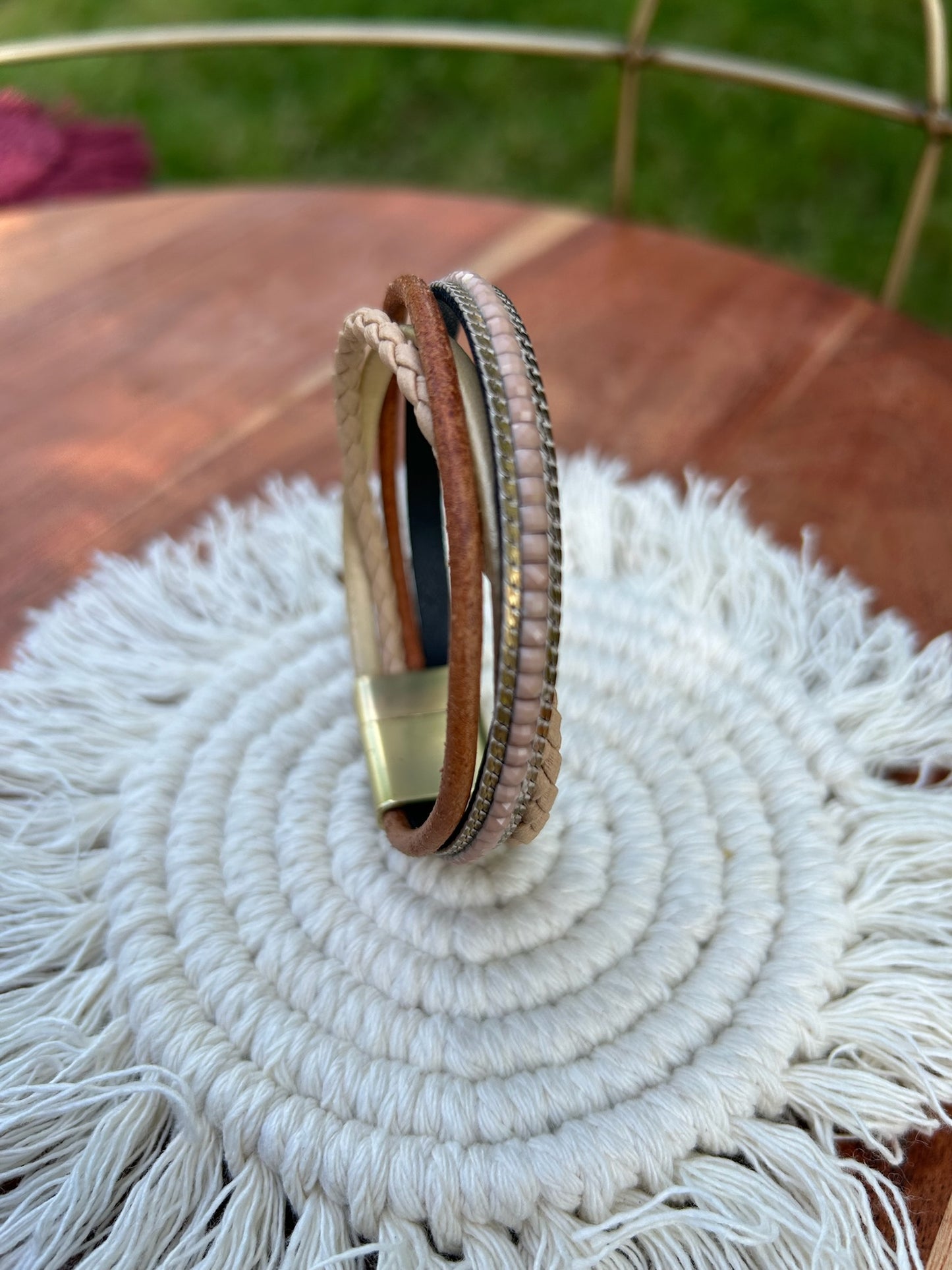 A close-up of a Crossroads bracelet from Canyon Jewelry featuring different textures and colors, displayed on a circular woven mat on a grassy background. This unique fashion accessory combines aesthetic appeal with intricate design.