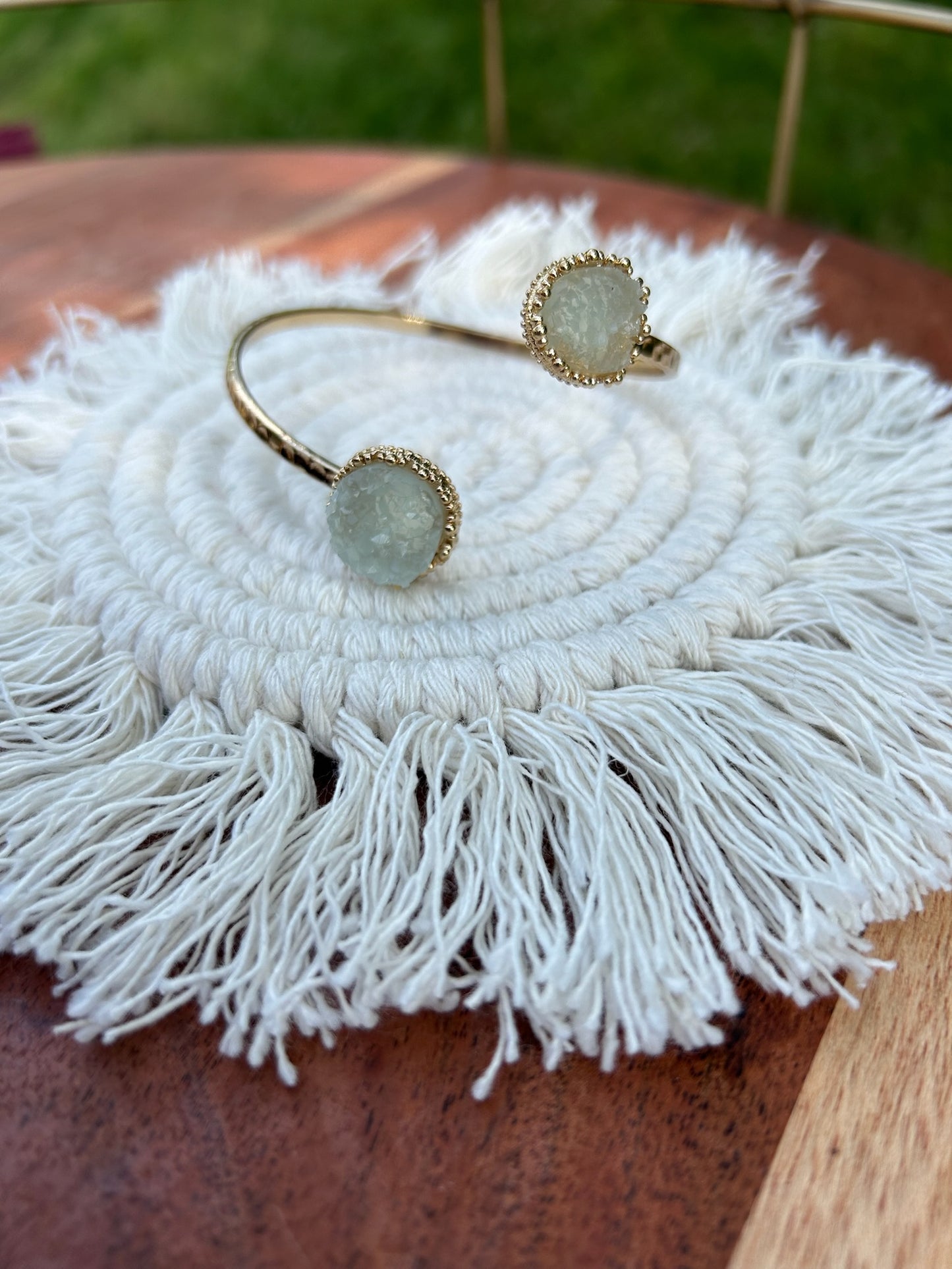 A close-up of a hand holding two Divergence Bracelets from Canyon Jewelry, with large, white, sparkly circular pendants, focuses against a softly blurred greenery background. These statement jewelry pieces capture attention effortlessly.