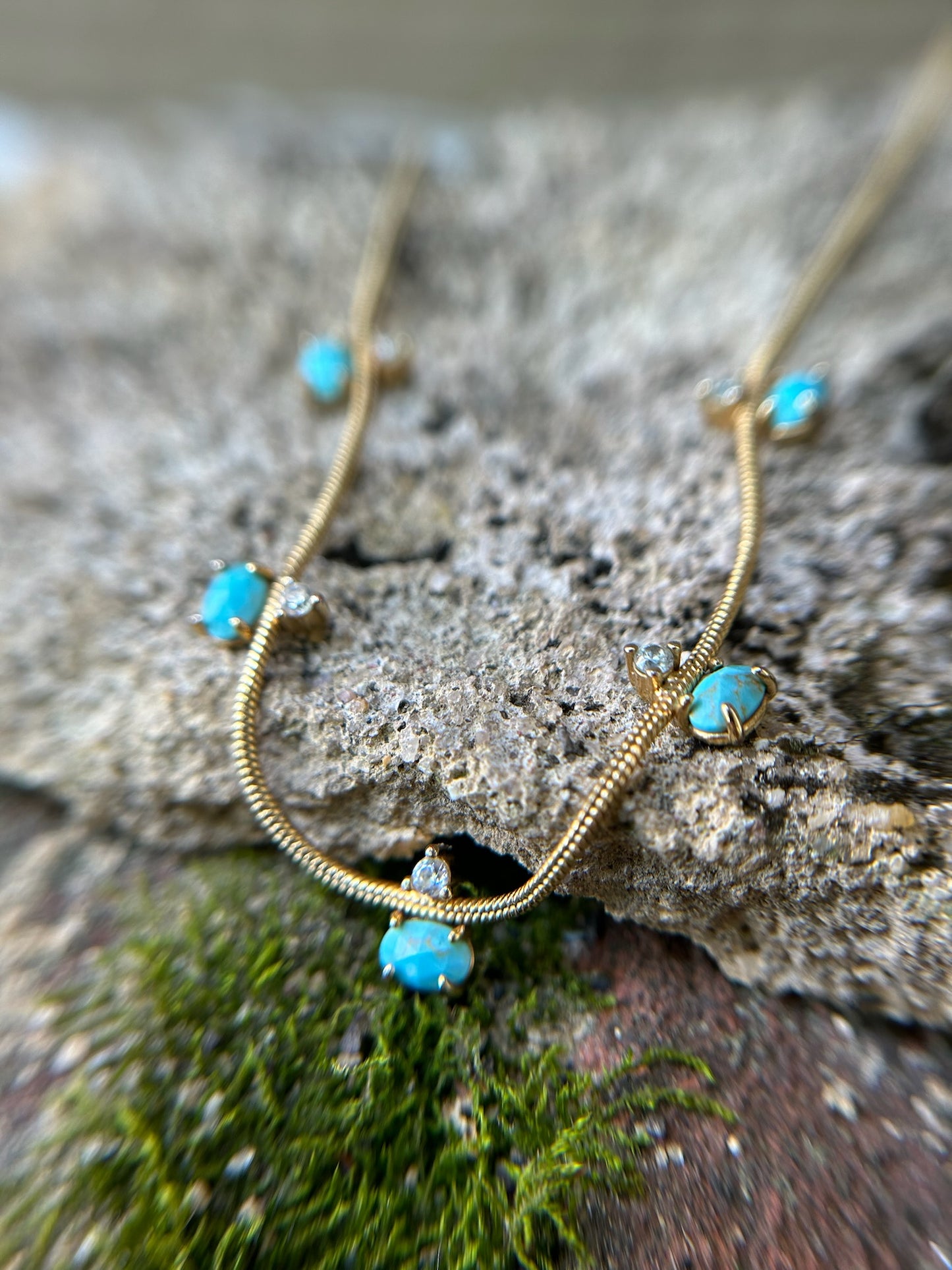 A delicate Canyon Jewelry Five Points Necklace with small turquoise stones and tiny diamond accents displayed on a wooden surface.