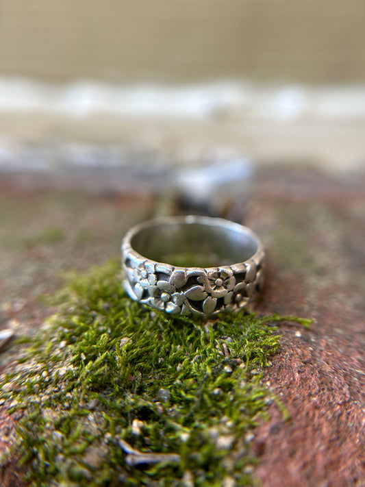 A close-up of a Flora Ring by Canyon Jewelry, a vintage silver ring with delicate flower engravings, resting on a bed of vibrant green moss with a soft, blurred background.