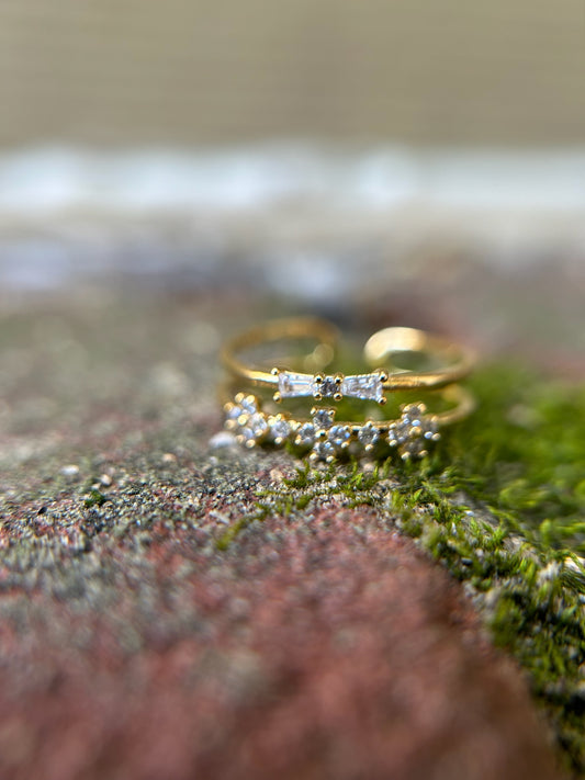 Close-up of two elegant Canyon Jewelry Mata Hari Rings with diamonds, placed on a textured surface that looks like moss, with a beautifully blurred background emphasizing the jewelry's sparkle.