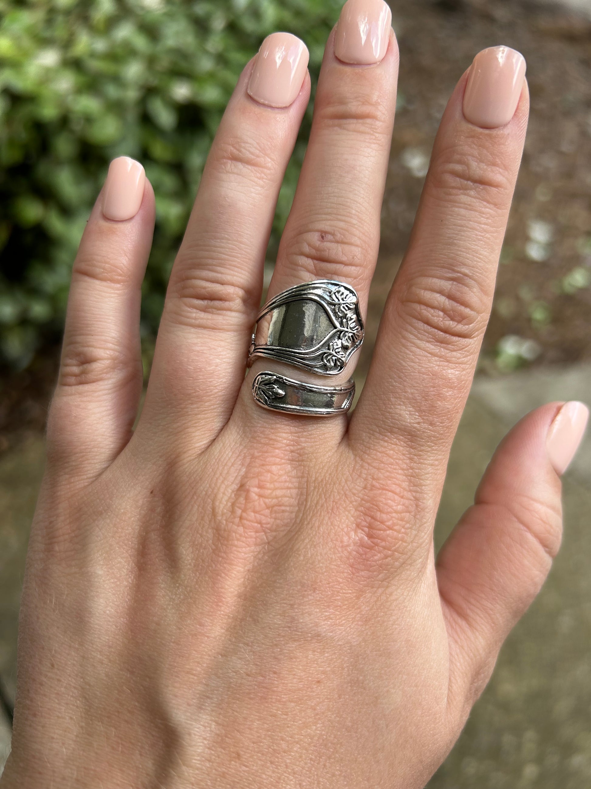 A detailed Cleopatra Spoon Ring from Canyon Jewelry, with ornate floral engravings, resting upright on a bed of green moss with a blurred background, evoking the charm of vintage jewelry.