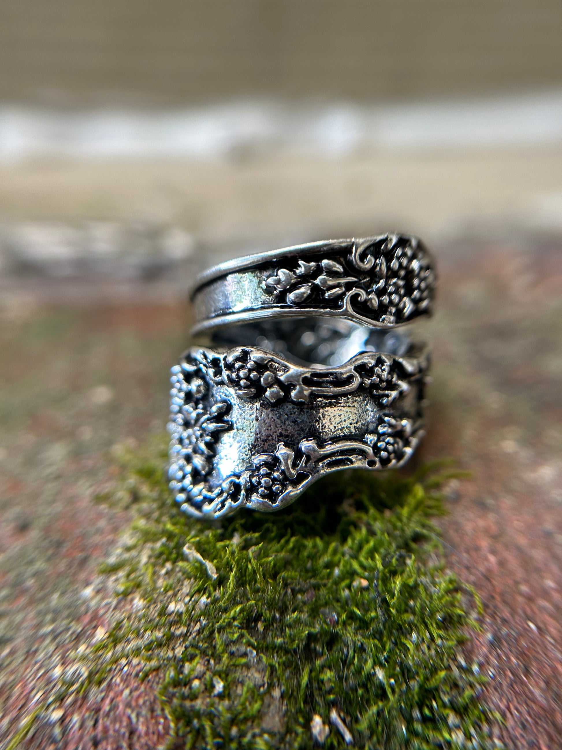 Close-up of an intricately detailed Canyon Jewelry Antoinette Spoon Ring with floral patterns, resting on a vibrant green mossy surface.