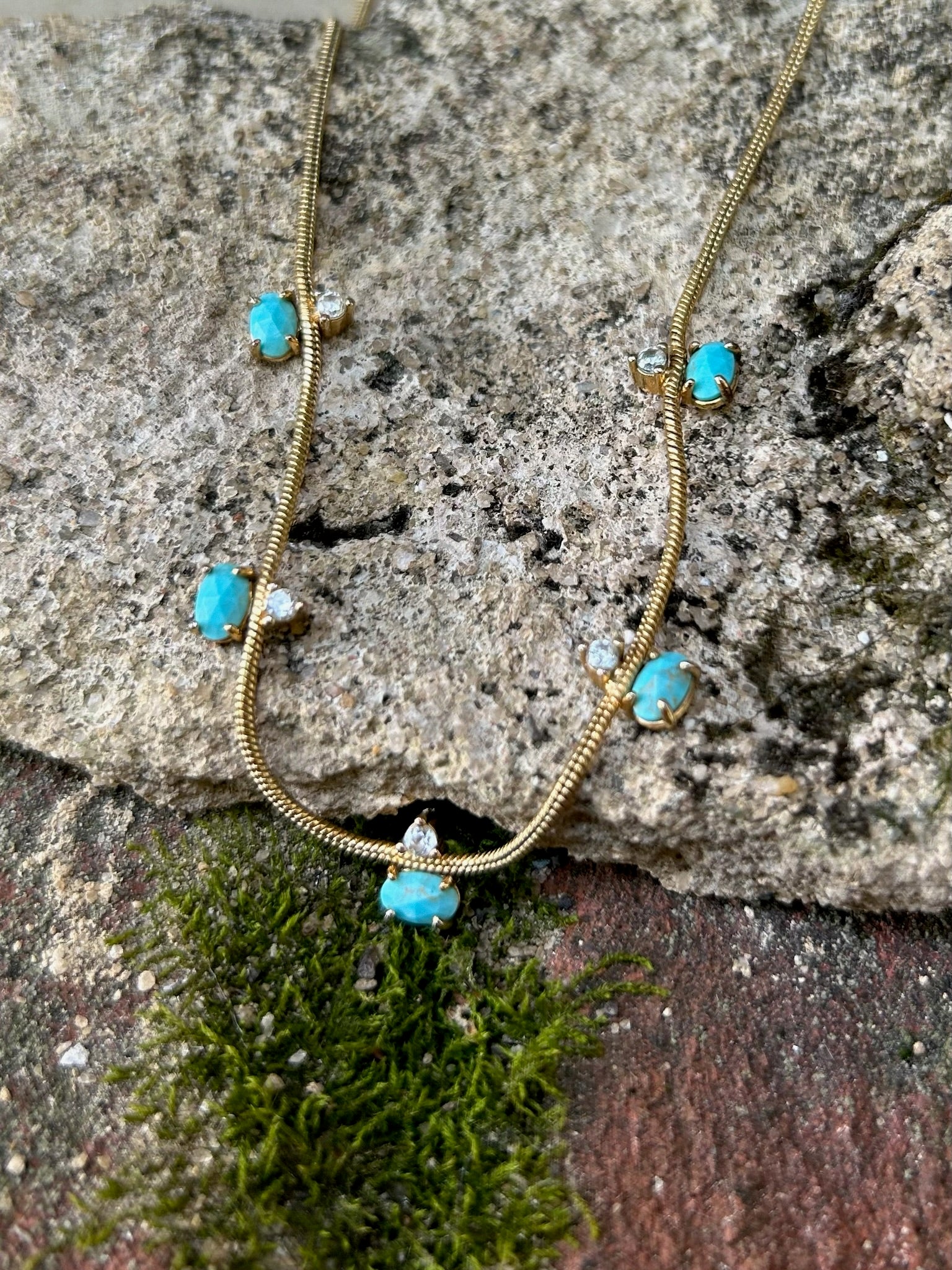 A delicate Canyon Jewelry Five Points Necklace with small turquoise stones and tiny diamond accents displayed on a wooden surface.