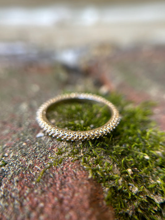 A close-up image of a Rough-Around-the-Edges Ring from Canyon Jewelry, with small clear gemstones, placed on a moss-covered rock surface, showcasing its vintage jewelry charm against a soft-focus background.