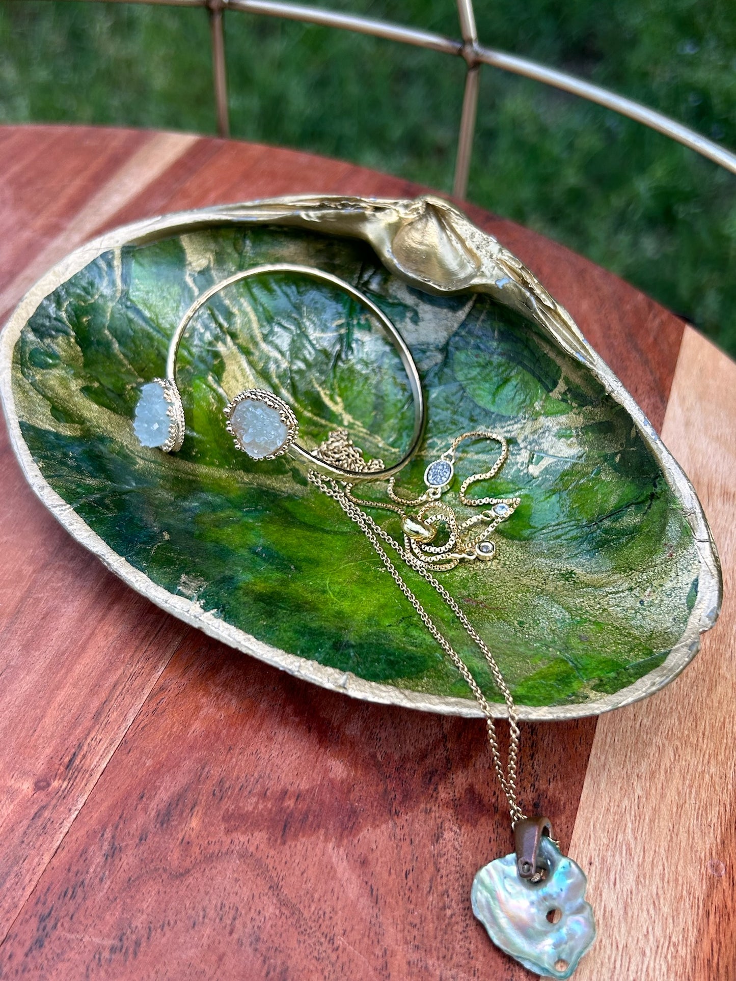 A decorative ceramic dish shaped and painted to resemble a green leaf with vein details, displayed on a sterling silver surface. The Canyon Jewelry Green Shell Trinket Tray has subtle golden accents along the edge and handle.