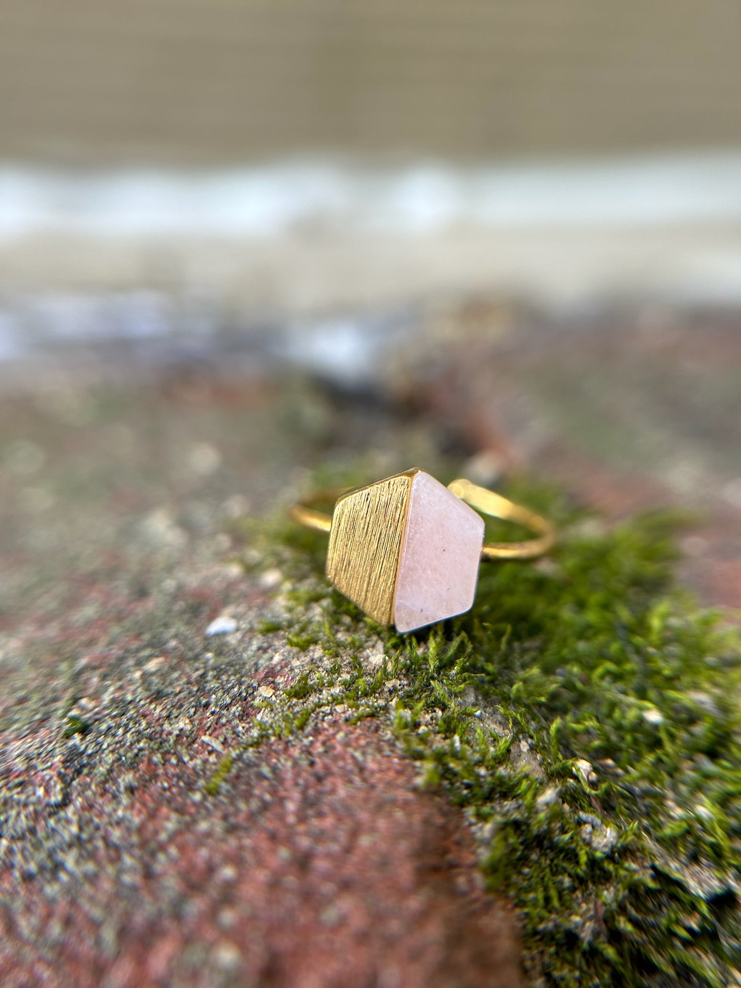 Close-up of a delicate Canyon Jewelry Josephine Ring with a hexagonal pink gemstone, set against a background of green moss and blurred surroundings.