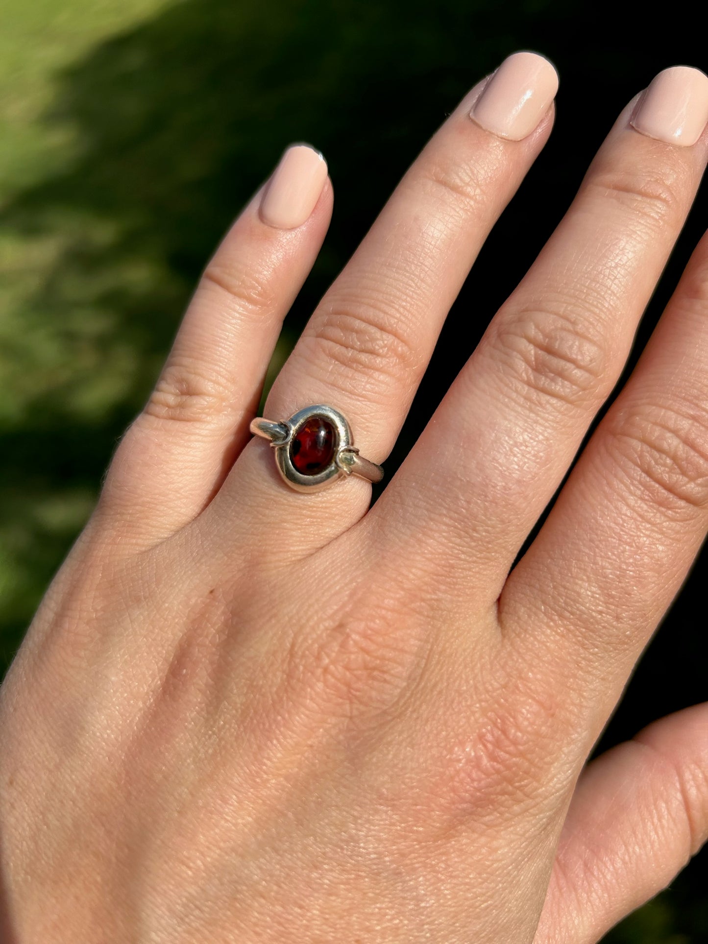 Close-up image of a vintage Ladybug Ring from Canyon Jewelry with an amber gemstone, set against a background of moss-covered stone. The focus is sharp on the gemstone, highlighting its rich, deep color.