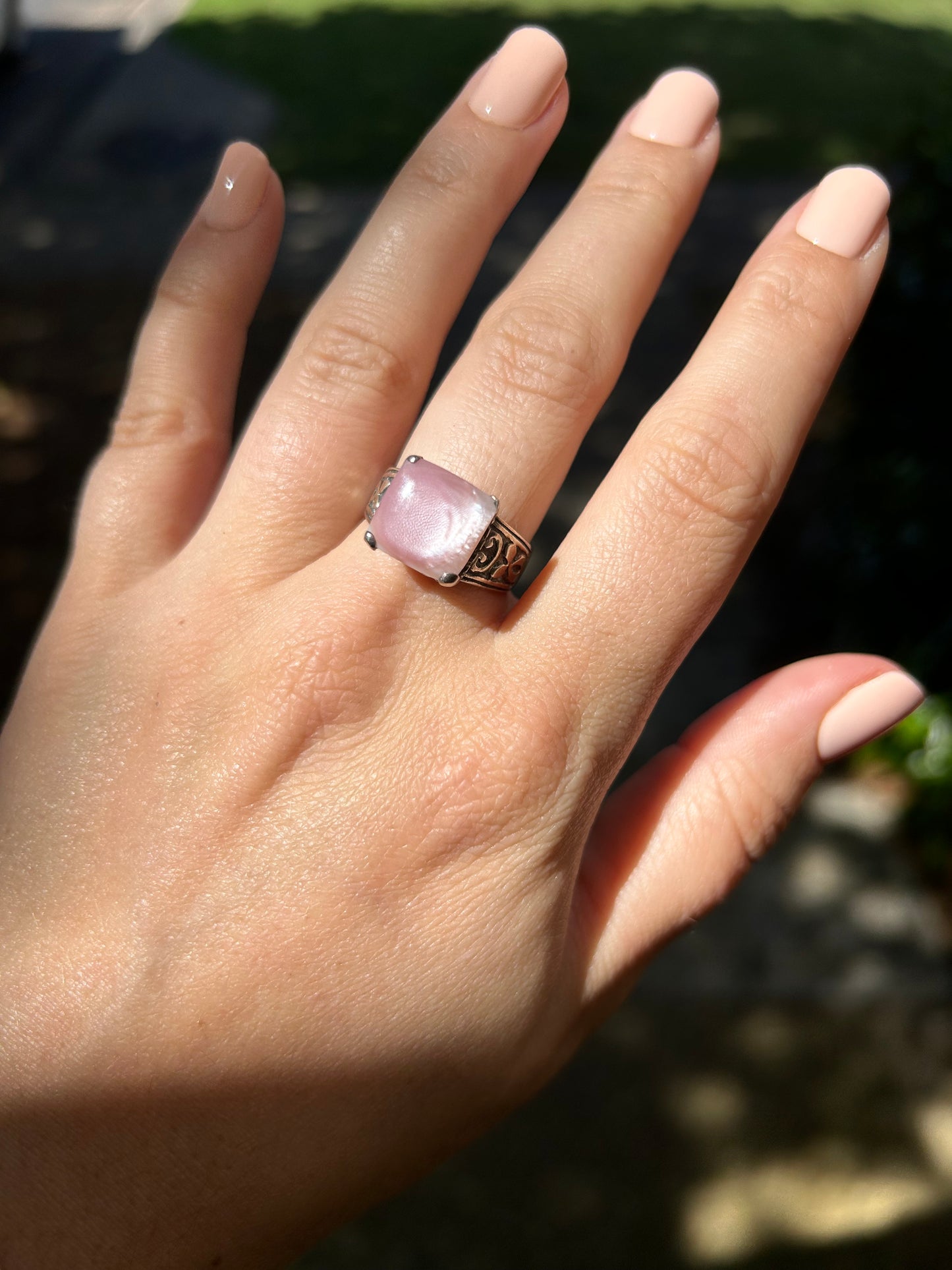 Close-up of a Canyon Jewelry Pink Marshmallow Ring with intricate metalwork, resting on a moss-covered surface with soft focus in the background.