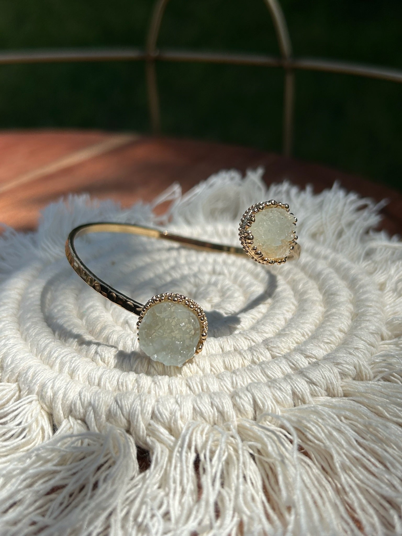 A close-up of a hand holding two Divergence Bracelets from Canyon Jewelry, with large, white, sparkly circular pendants, focuses against a softly blurred greenery background. These statement jewelry pieces capture attention effortlessly.