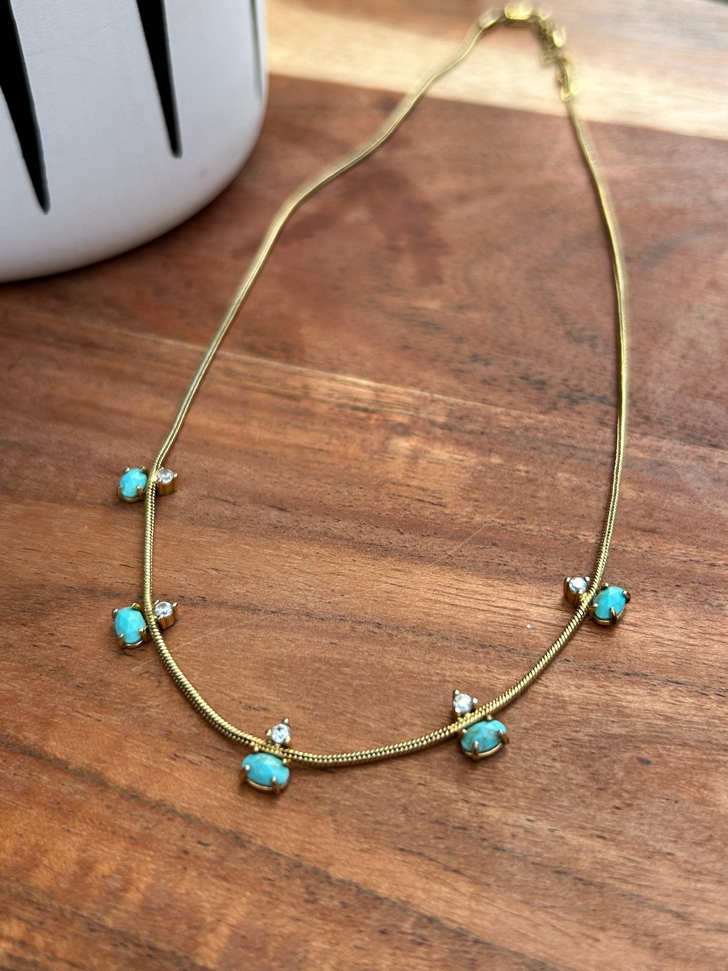 A delicate Canyon Jewelry Five Points Necklace with small turquoise stones and tiny diamond accents displayed on a wooden surface.