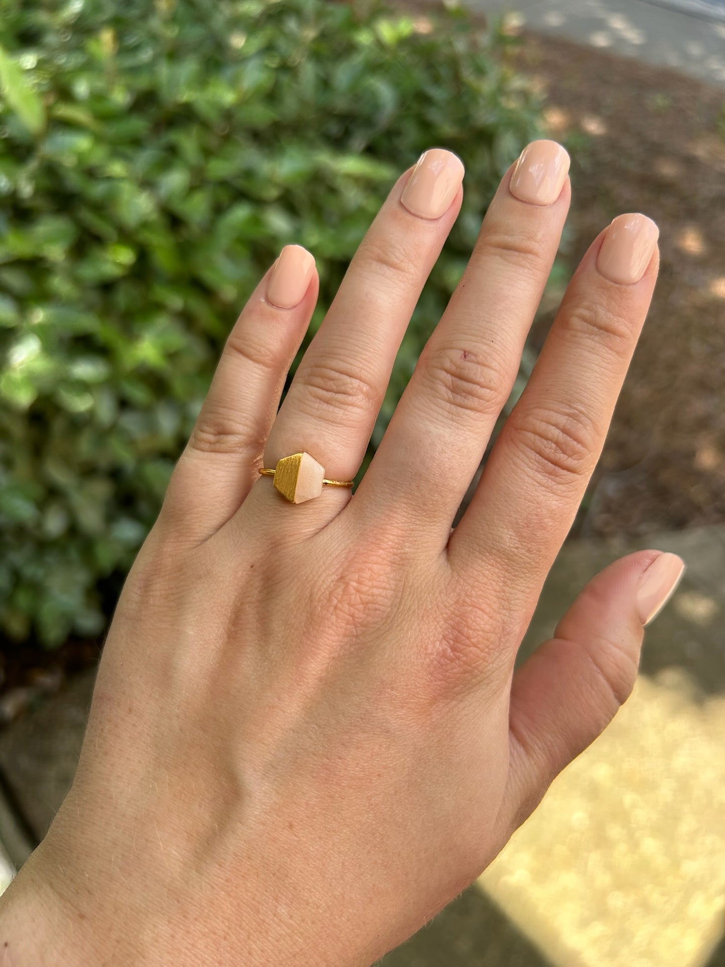 Close-up of a delicate Canyon Jewelry Josephine Ring with a hexagonal pink gemstone, set against a background of green moss and blurred surroundings.