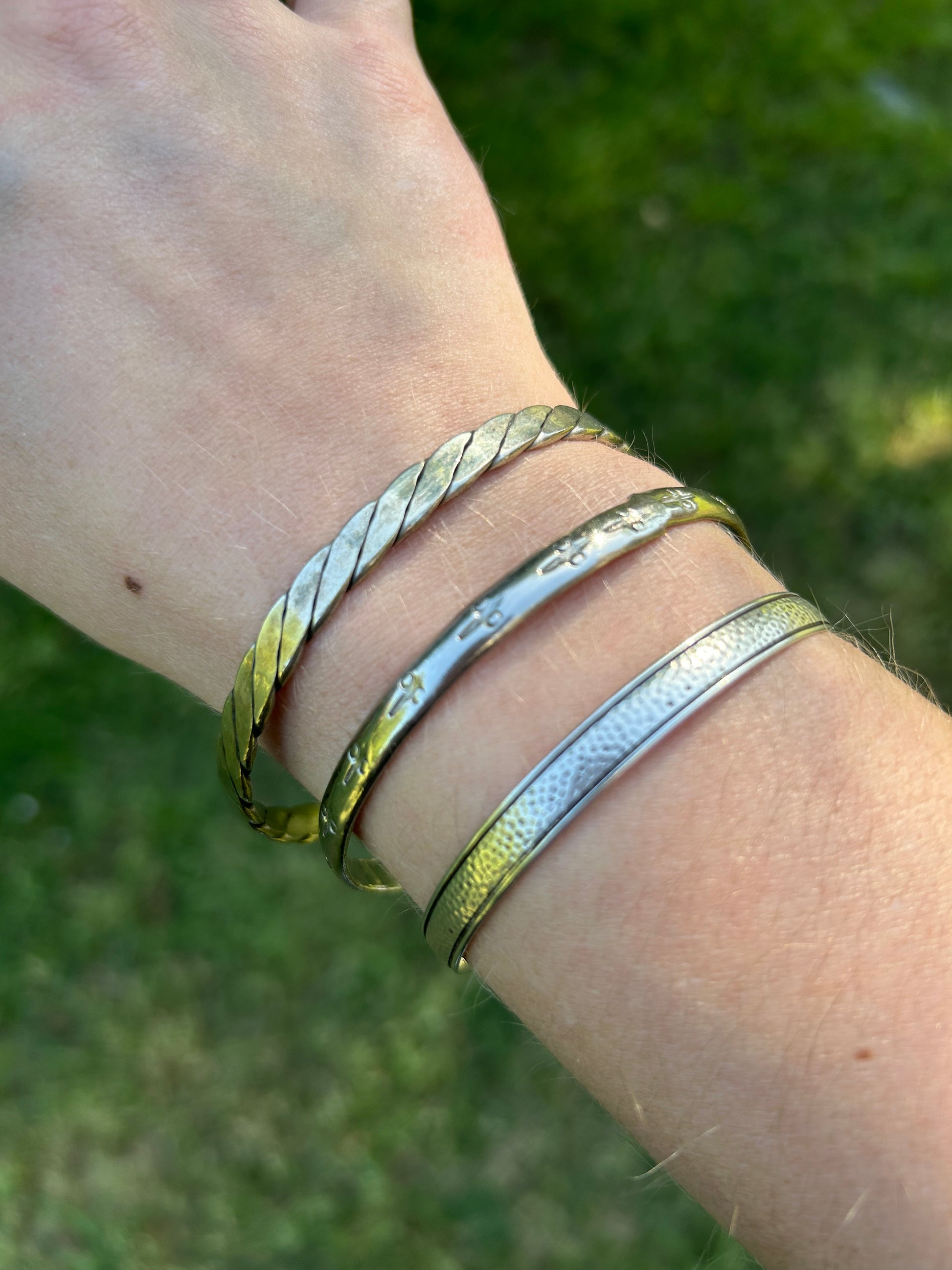 A Canyon Jewelry Lasso Bangle, a piece of western jewelry, rests on a textured burgundy tasseled rug, partially shaded by the edge of a white object, with sunlit grass visible in the background.