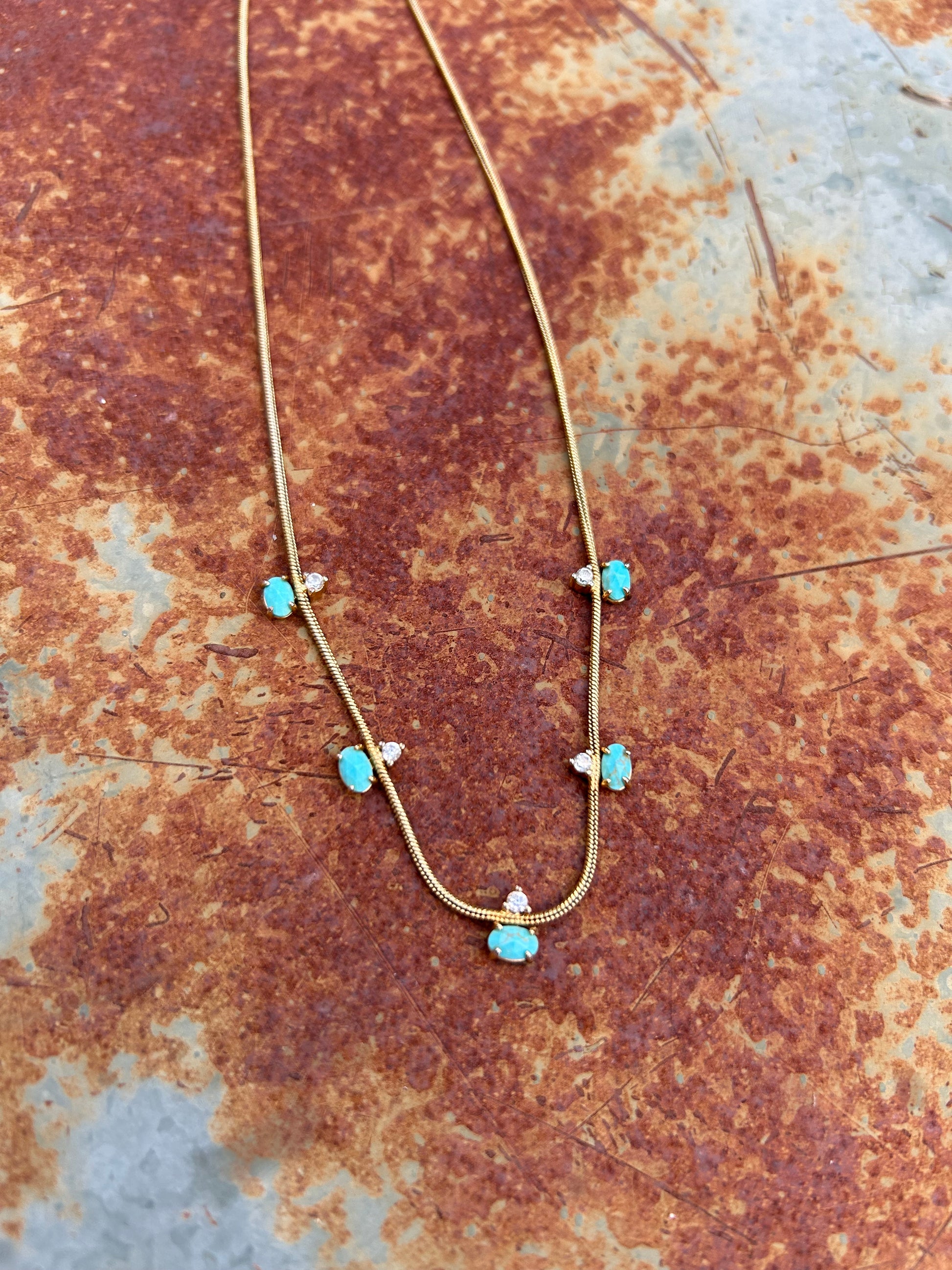 A delicate Canyon Jewelry Five Points Necklace with small turquoise stones and tiny diamond accents displayed on a wooden surface.