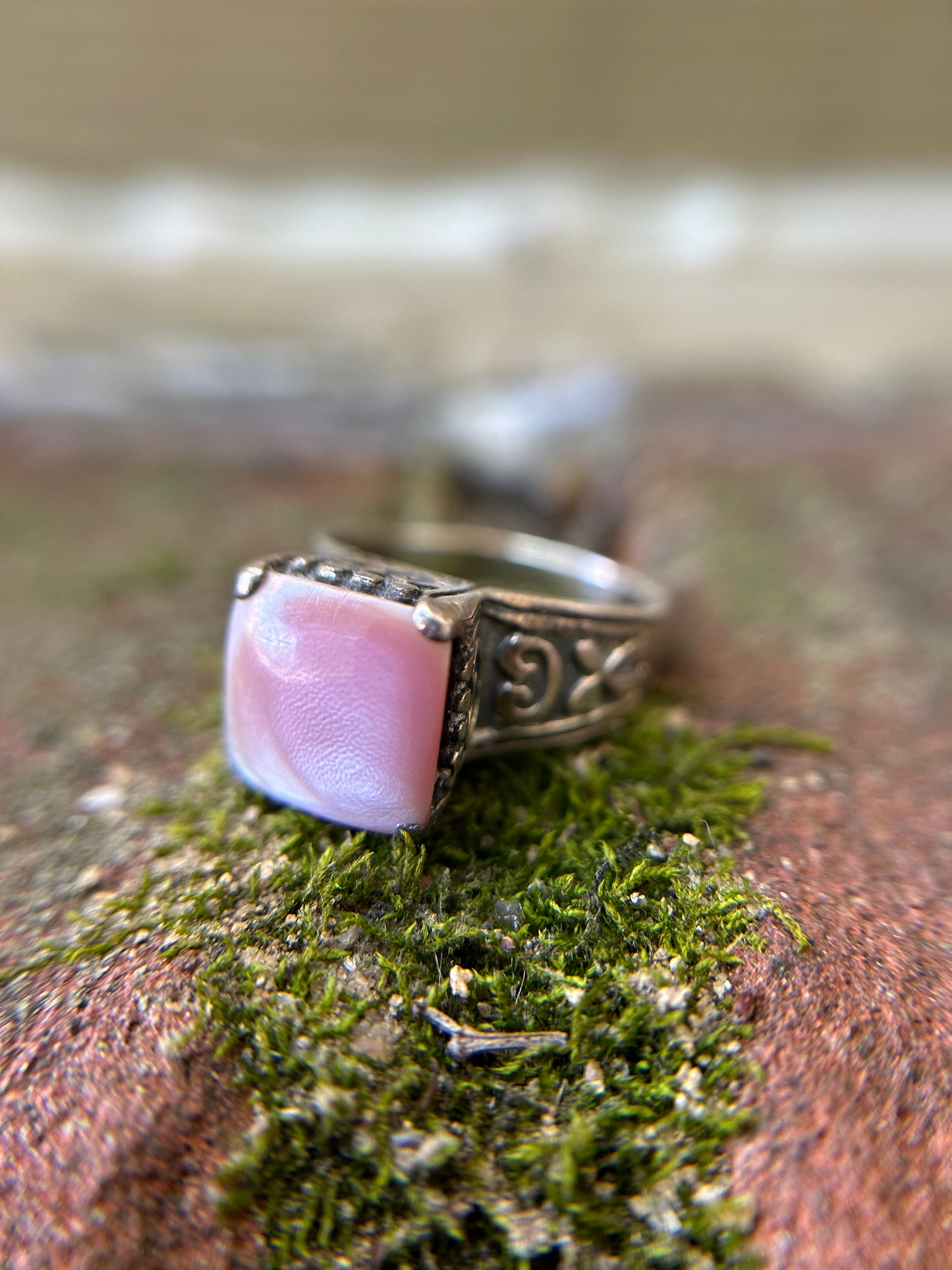 Close-up of a Canyon Jewelry Pink Marshmallow Ring with intricate metalwork, resting on a moss-covered surface with soft focus in the background.