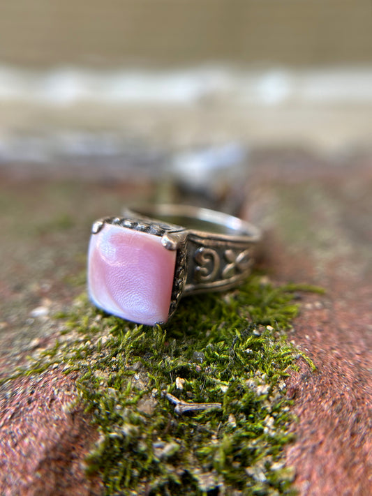 Close-up of a Canyon Jewelry Pink Marshmallow Ring with intricate metalwork, resting on a moss-covered surface with soft focus in the background.