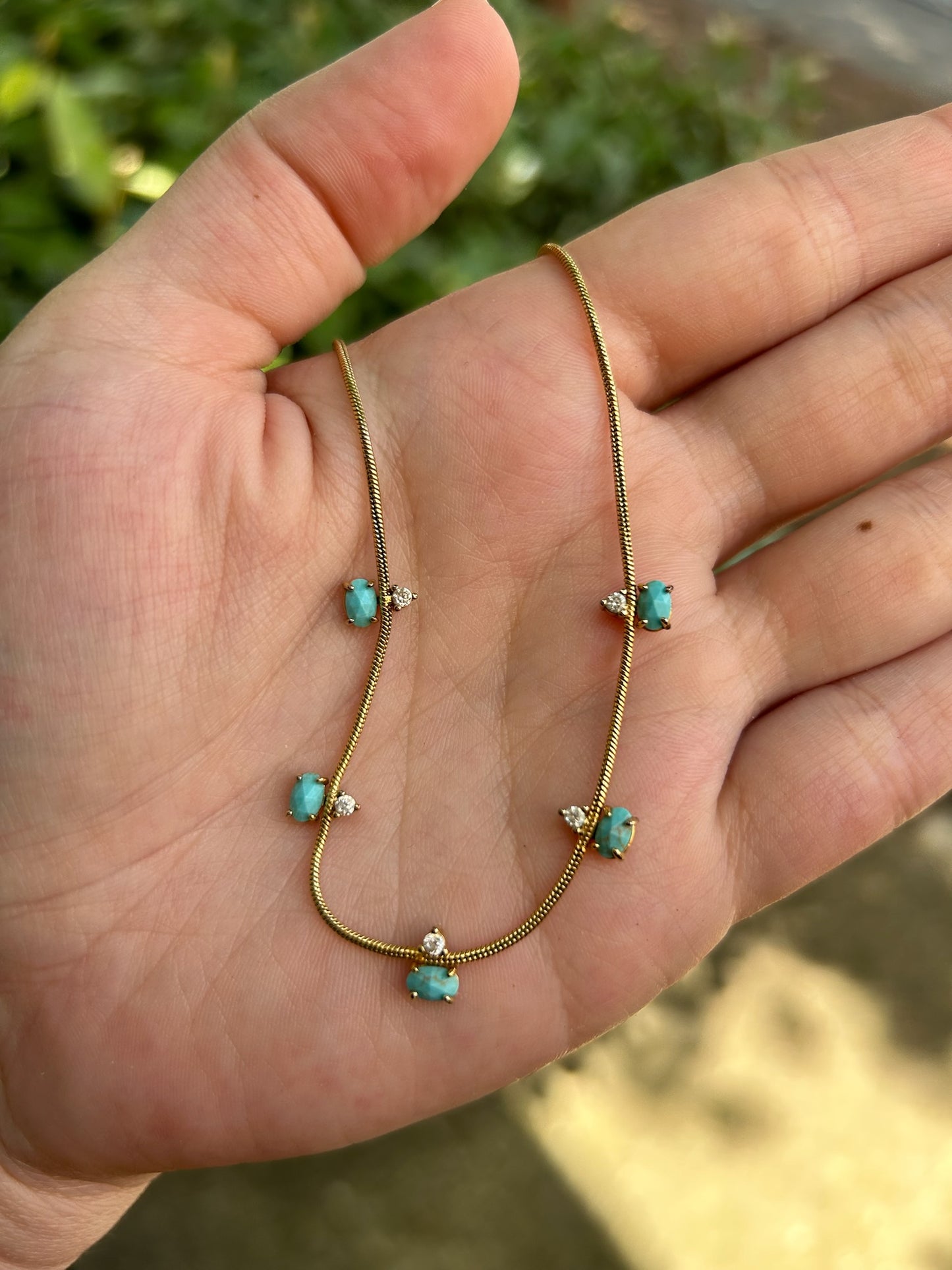 A delicate Canyon Jewelry Five Points Necklace with small turquoise stones and tiny diamond accents displayed on a wooden surface.