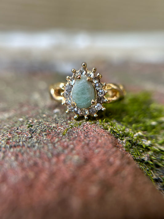 A close-up of an elegant Canyon Jewelry Pastel Pasture Ring with an oval aquamarine stone surrounded by small diamonds, resting on a moss-covered stone surface.