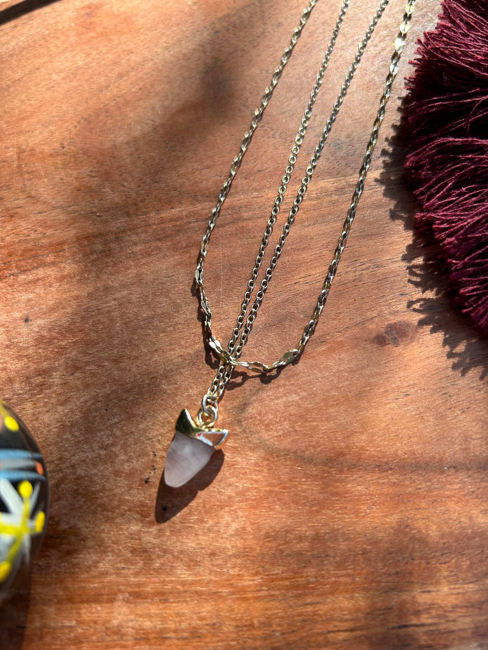 Close-up of a Great White Necklace featuring a white shark tooth encased in gold, suspended on a sterling silver chain, resting on a mossy surface by Canyon Jewelry.