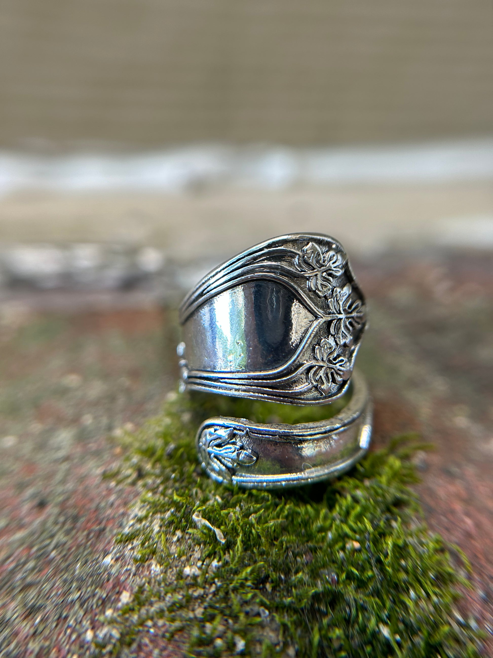 A detailed Cleopatra Spoon Ring from Canyon Jewelry, with ornate floral engravings, resting upright on a bed of green moss with a blurred background, evoking the charm of vintage jewelry.