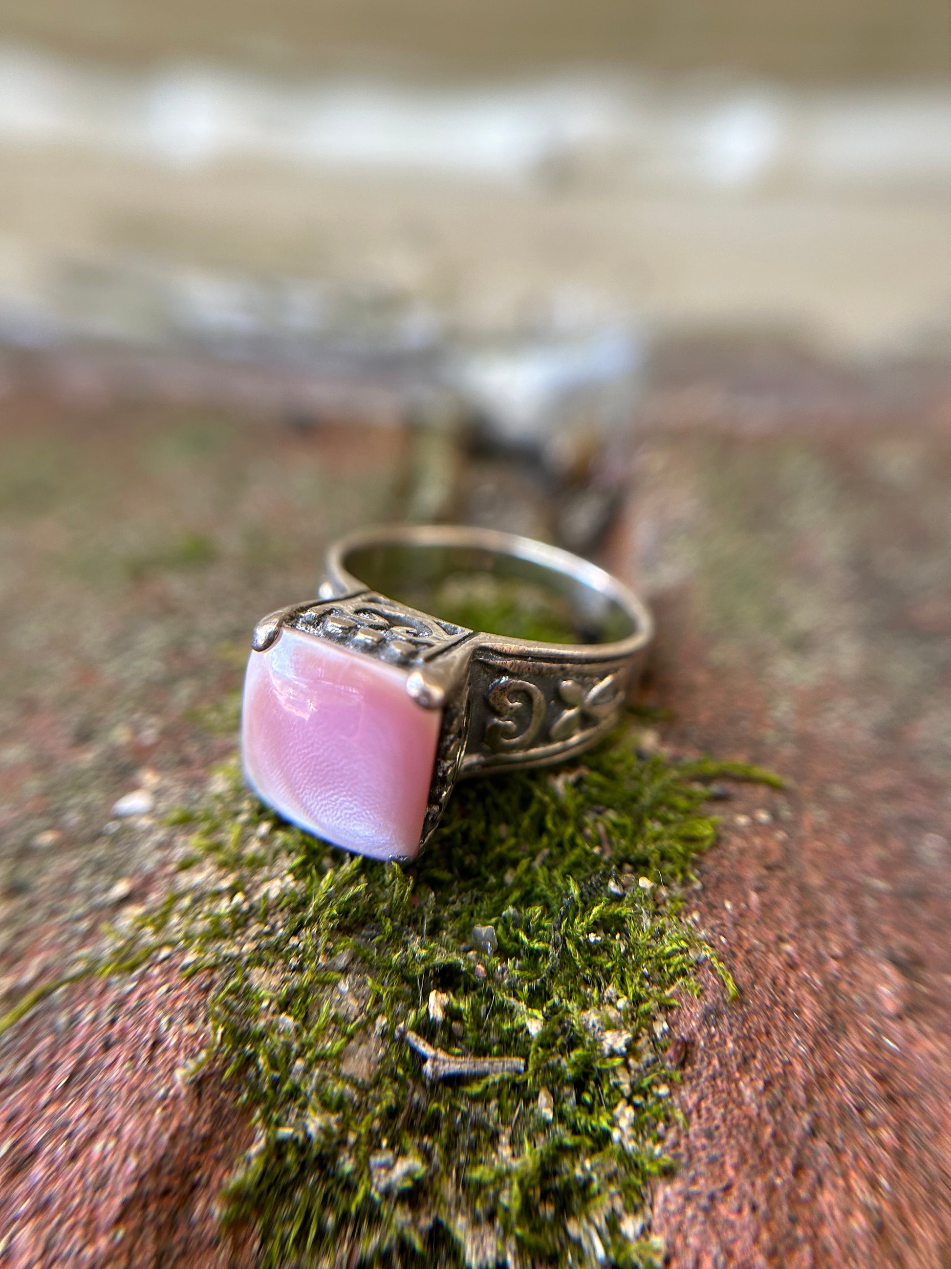 Close-up of a Canyon Jewelry Pink Marshmallow Ring with intricate metalwork, resting on a moss-covered surface with soft focus in the background.