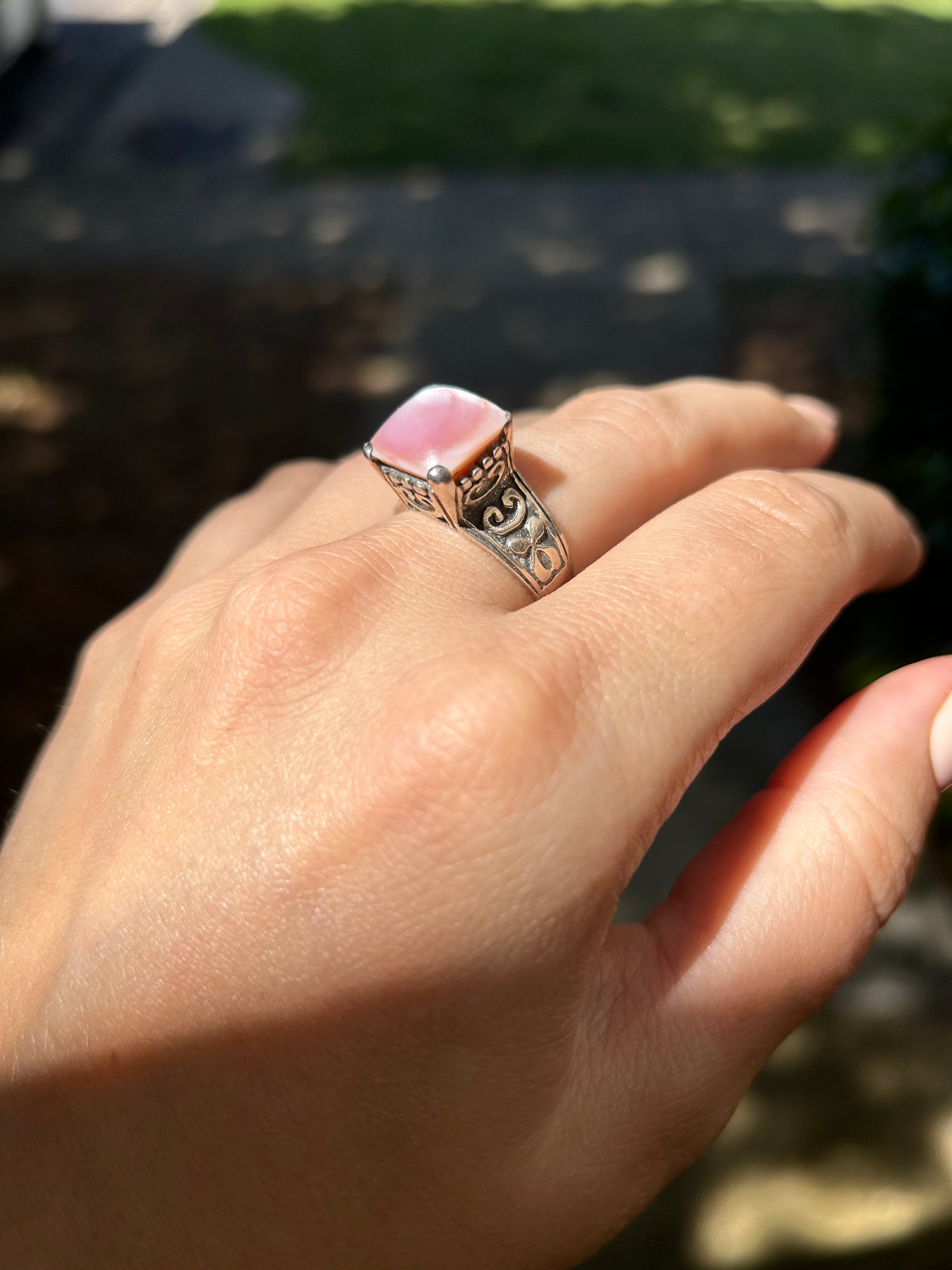 Close-up of a Canyon Jewelry Pink Marshmallow Ring with intricate metalwork, resting on a moss-covered surface with soft focus in the background.