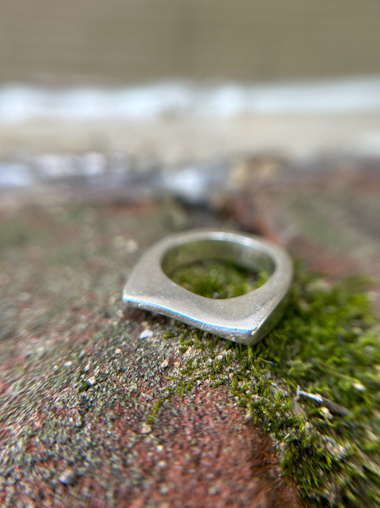 Close-up of a Manifest ring by Canyon Jewelry embedded in a moss-covered stone surface, showcasing fine details and boho textures with a blurred background.