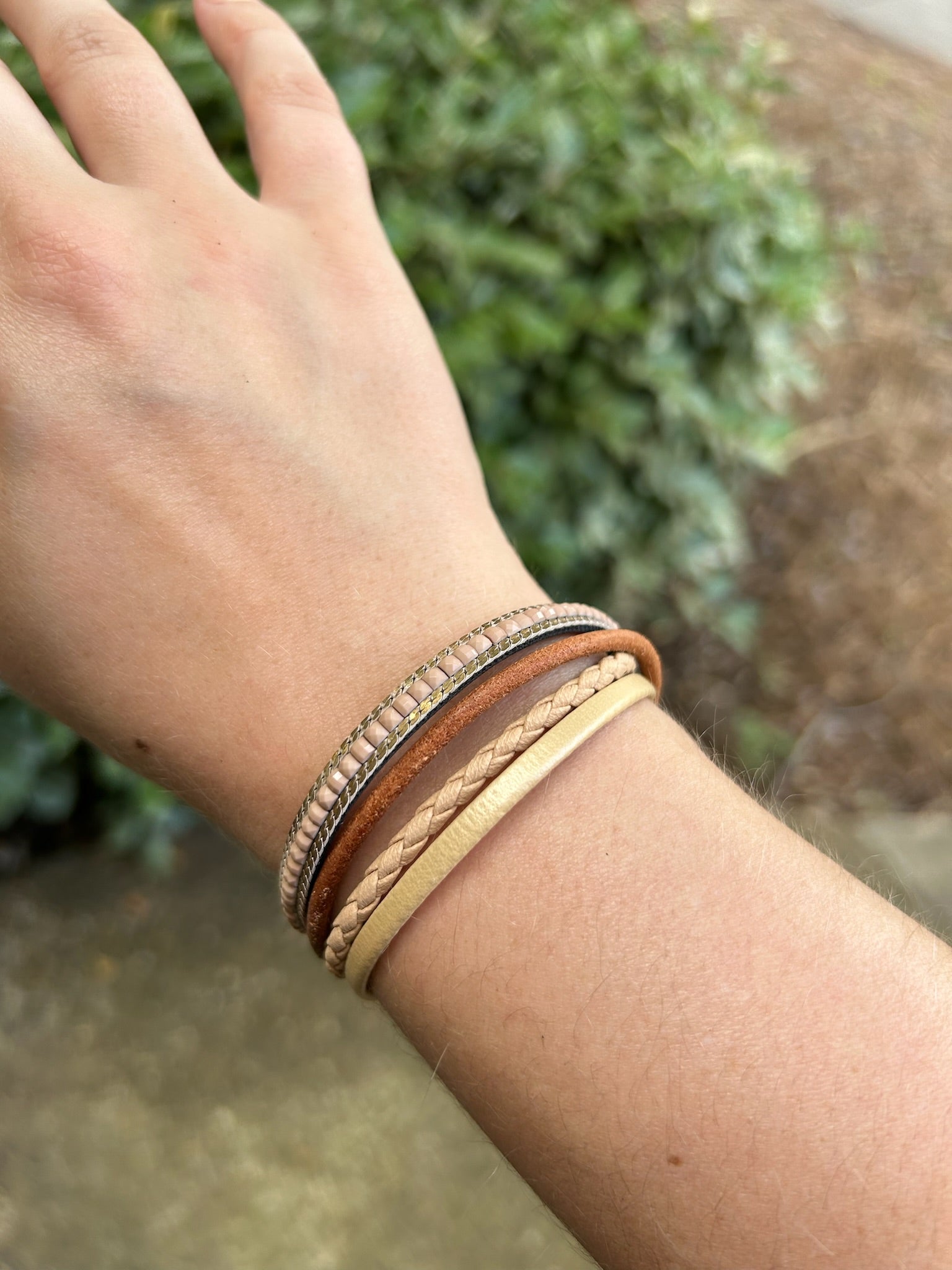 A close-up of a Crossroads bracelet from Canyon Jewelry featuring different textures and colors, displayed on a circular woven mat on a grassy background. This unique fashion accessory combines aesthetic appeal with intricate design.