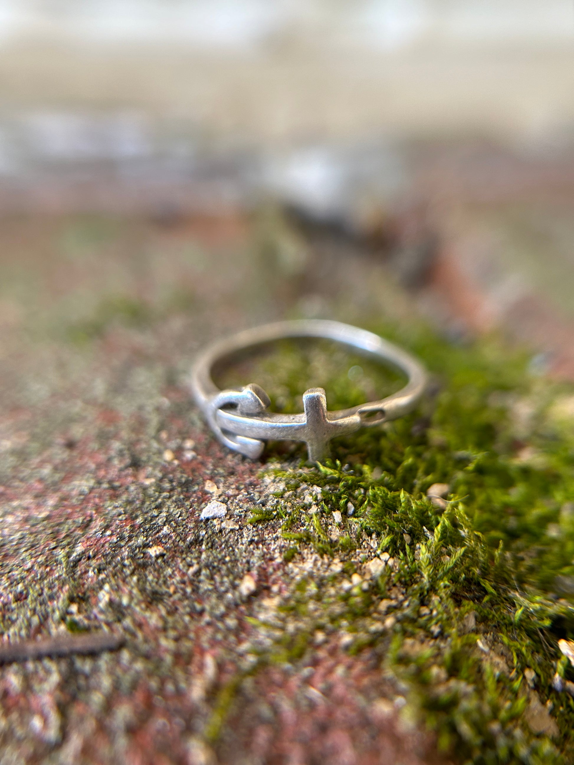 Close-up of a Canyon Jewelry anchor ring with a peace symbol design resting on a moss-covered surface, with a soft focus background.