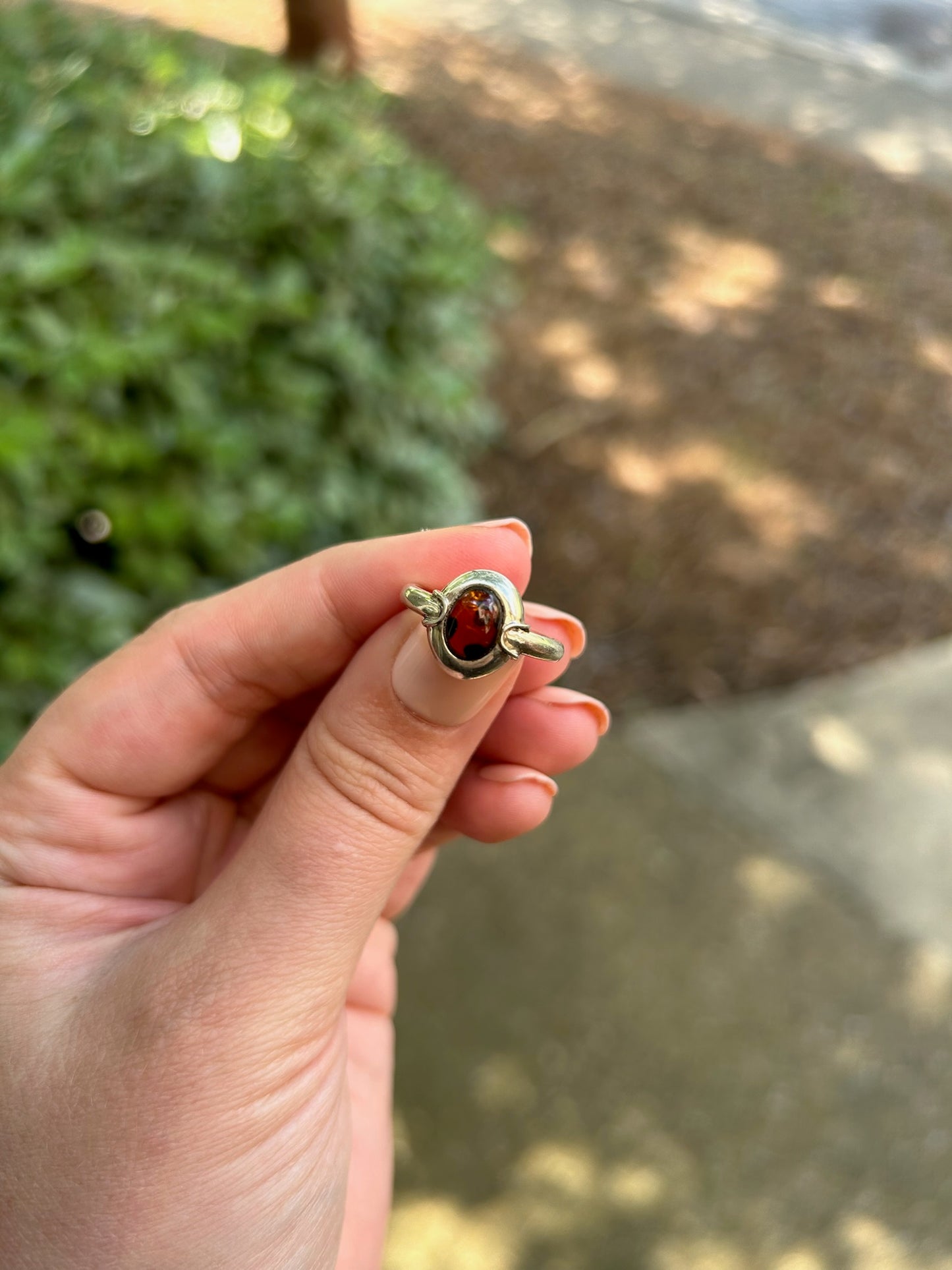 Close-up image of a vintage Ladybug Ring from Canyon Jewelry with an amber gemstone, set against a background of moss-covered stone. The focus is sharp on the gemstone, highlighting its rich, deep color.