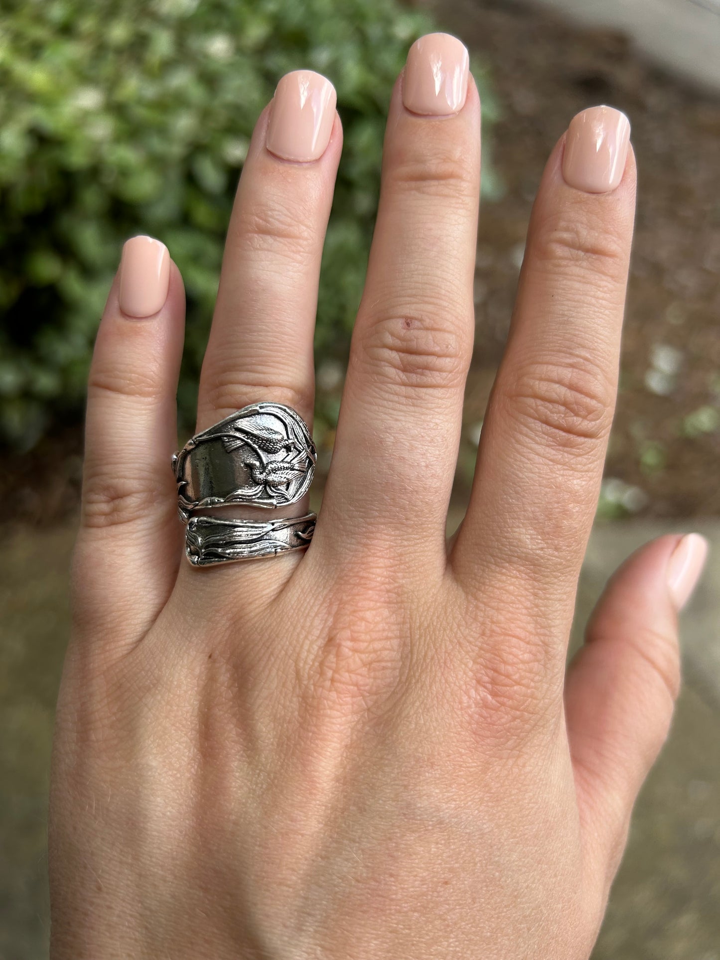 Close-up image of a Audrey Spoon Ring from Canyon Jewelry with intricate dragon engravings, resting on a mossy surface, with a blurred background.