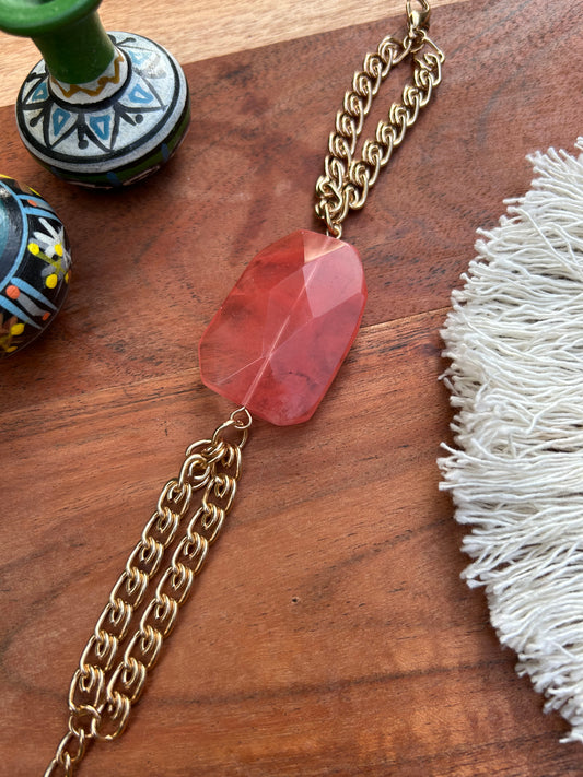 A Hillier Bracelet on a golden chain, resting on a wooden surface next to decorative ceramic vases and a white fringed boho cloth.