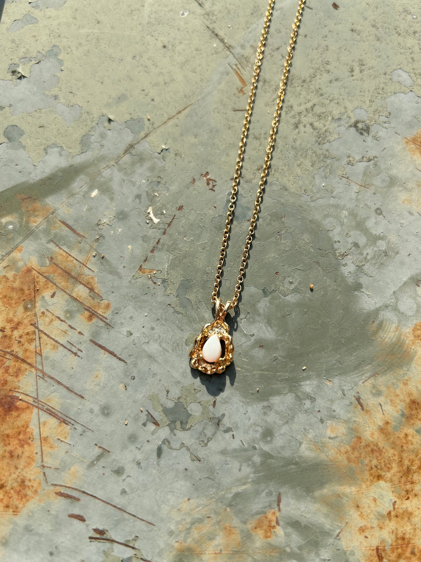 A delicate Canyon Jewelry gold Teardrop Necklace with a white oval pendant rests on a wooden surface beside a colorful boho ceramic vase and a white fringed textile.